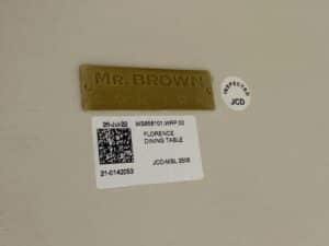 A sticker reads "Mr. Brown London Florence Dining Table," placed on a beige surface with an inspection label.