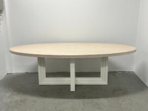 The Mr. Brown London Florence Dining Table features an oval wooden top with a light hue and a geometric white base, perfect for a minimalist room setting.