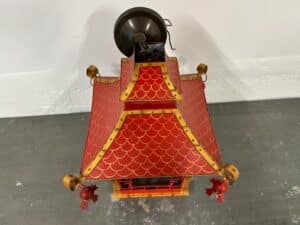 Red and gold pagoda-shaped lantern with a scalloped roof pattern and decorative corner tassels.
