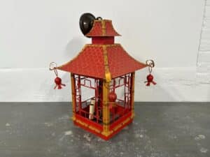 Red and gold lantern with ornate roof and hanging ornaments against a plain background.