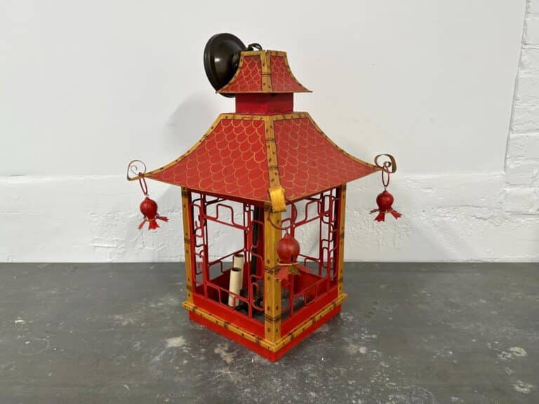 Red and gold lantern with ornate roof and hanging ornaments against a plain background.