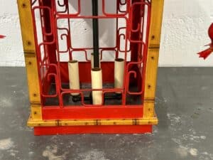 Red and gold decorative lantern with three candle holders inside, placed on a gray surface.