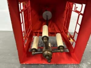 Inside view of a red, open metal framework with a central rod and cylindrical components, resembling a vintage lantern.
