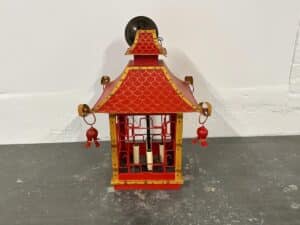 Red decorative lantern with gold accents and tassels, shaped like a pagoda, against a plain background.