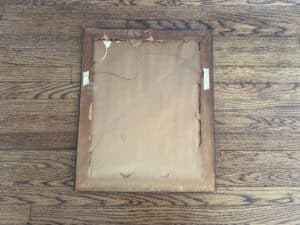 Damaged wooden frame with a worn look, containing the "Birds of Paradise Painting, Signed Lower Right," rests on a hardwood floor.