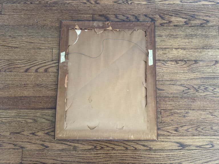 Damaged wooden frame with a worn look, containing the "Birds of Paradise Painting, Signed Lower Right," rests on a hardwood floor.