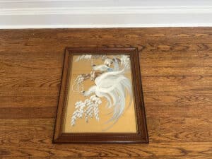 The Birds of Paradise Painting, signed on the lower right, features a white bird surrounded by flowers and is displayed on a wooden floor.