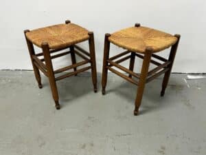A pair of Rush Stools with woven seats is placed on a concrete floor against a white wall.