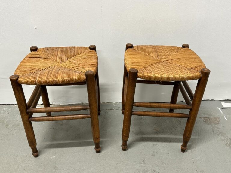 A pair of Rush Stools with woven straw seats sit on a gray floor against a white wall.