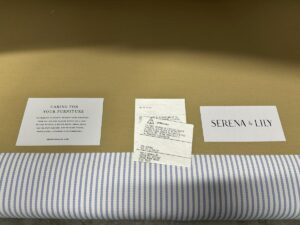 Care instructions and a Serena & Lily card are placed on the fabric surface of the beige and striped blue Serena & Lily Barton Sofa.