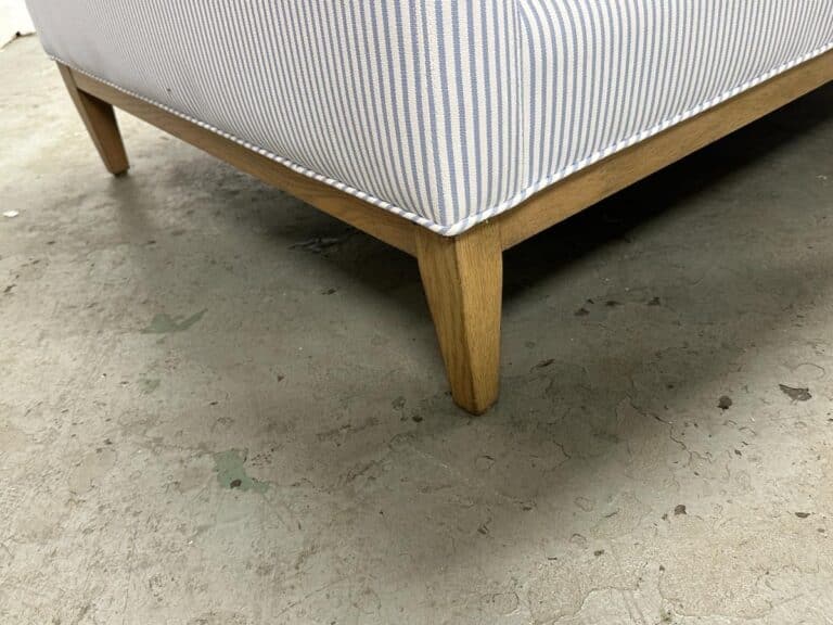 Close-up of the Serena & Lily Barton Sofa, featuring stripes and wooden legs, on a cracked concrete floor.