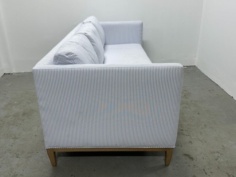 Side view of the Serena & Lily Barton Sofa, featuring white and light blue stripes and wooden legs, in a minimalistic room.