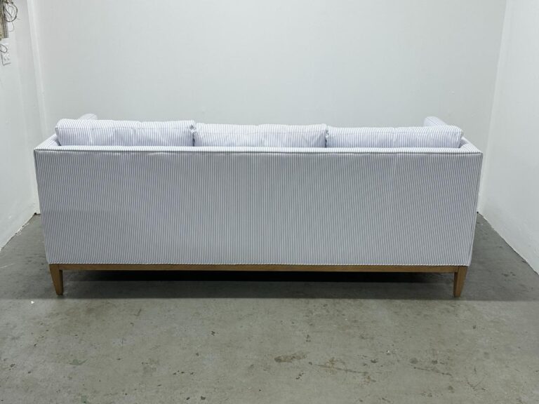 The Serena & Lily Barton Sofa features a back view showcasing light gray stripes and wooden legs, set in a white room.