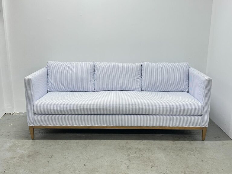 A Serena & Lily Barton Sofa in light blue with stripes and wooden legs sits against a plain white wall.