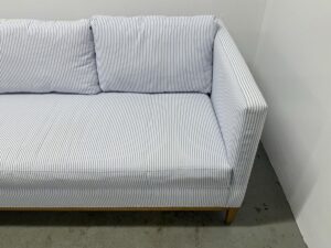 The Serena & Lily Barton Sofa, featuring blue and white stripes and paired with two cushions, is set against a plain white wall on a concrete floor.