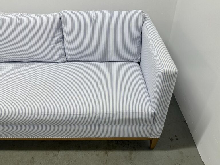 The Serena & Lily Barton Sofa, featuring blue and white stripes and paired with two cushions, is set against a plain white wall on a concrete floor.