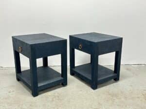Against a plain white wall, a pair of Serena & Lily Driftway Dark Blue One-Drawer Nightstands stands, featuring dark wood and bottom shelves.