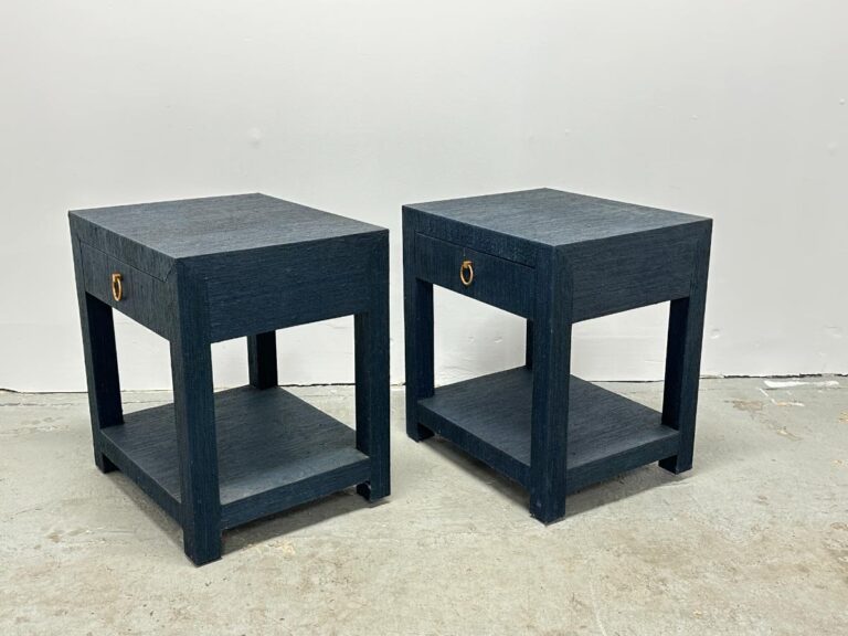 Against a plain white wall, a pair of Serena & Lily Driftway Dark Blue One-Drawer Nightstands stands, featuring dark wood and bottom shelves.