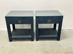 Against a plain wall stand two Serena & Lily Driftway one-drawer nightstands in dark blue, featuring brass handles and a lower shelf.