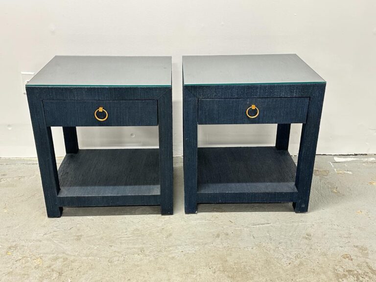Against a plain wall stand two Serena & Lily Driftway one-drawer nightstands in dark blue, featuring brass handles and a lower shelf.