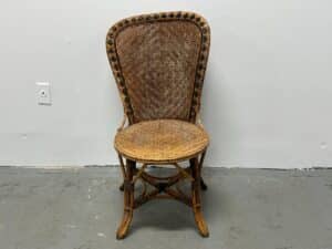A wicker chair with a decorative backrest against a white wall on a gray floor.