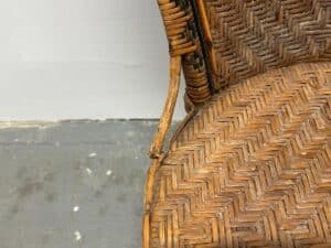 Damaged wicker chair with broken armrest on a gray, textured floor background.