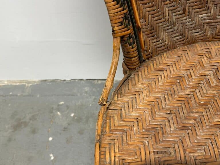 Damaged wicker chair with broken armrest on a gray, textured floor background.