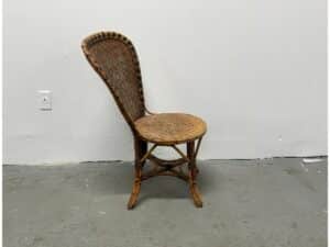Rattan chair with a high backrest against a plain white wall and gray floor.
