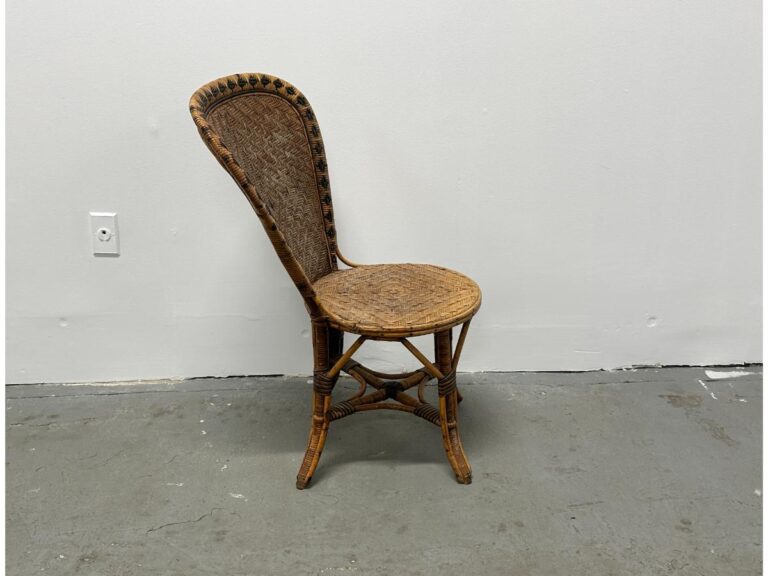 Rattan chair with a high backrest against a plain white wall and gray floor.