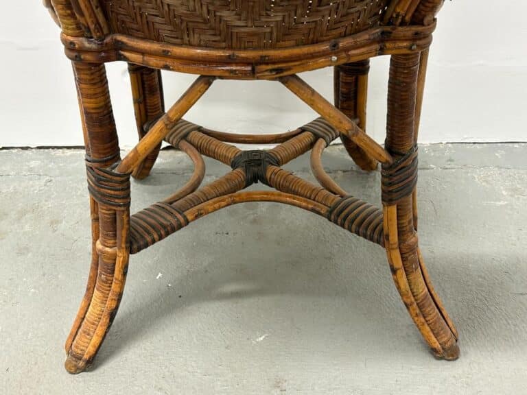 Wicker chair bottom with detailed weaving and curved legs, placed on a gray concrete floor.