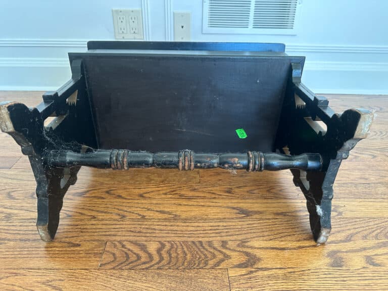 A wood carved storage bench with a green price sticker on a wooden floor.