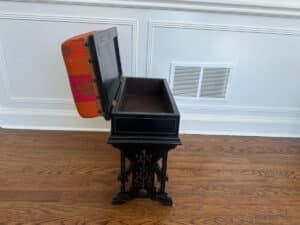 A Wood Carved Storage Bench featuring a decorative black music box with an open red-patterned lid on a wooden floor.