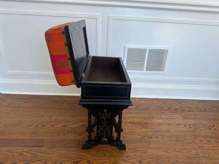A Wood Carved Storage Bench featuring a decorative black music box with an open red-patterned lid on a wooden floor.