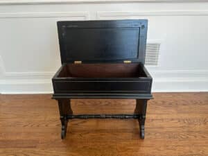 The Wood Carved Storage Bench, with an open lid and turned legs, stands on a hardwood floor.