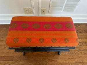 Wood Carved Storage Bench with red and orange patterned fabric on a wooden floor.
