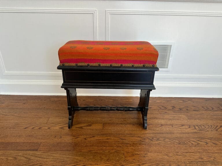 A black Wood Carved Storage Bench with an orange-red patterned cushion sits on a wooden floor against a white panel wall.
