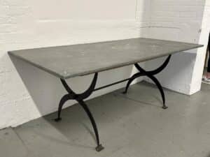 Rectangular metal table with curved iron legs against a white brick wall.