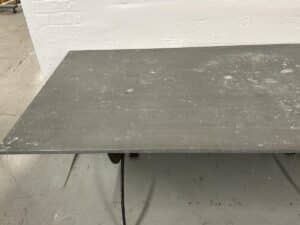 A large, worn metal sheet on a wheeled stand against a white wall in a workshop setting.