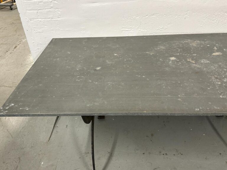 A large, worn metal sheet on a wheeled stand against a white wall in a workshop setting.