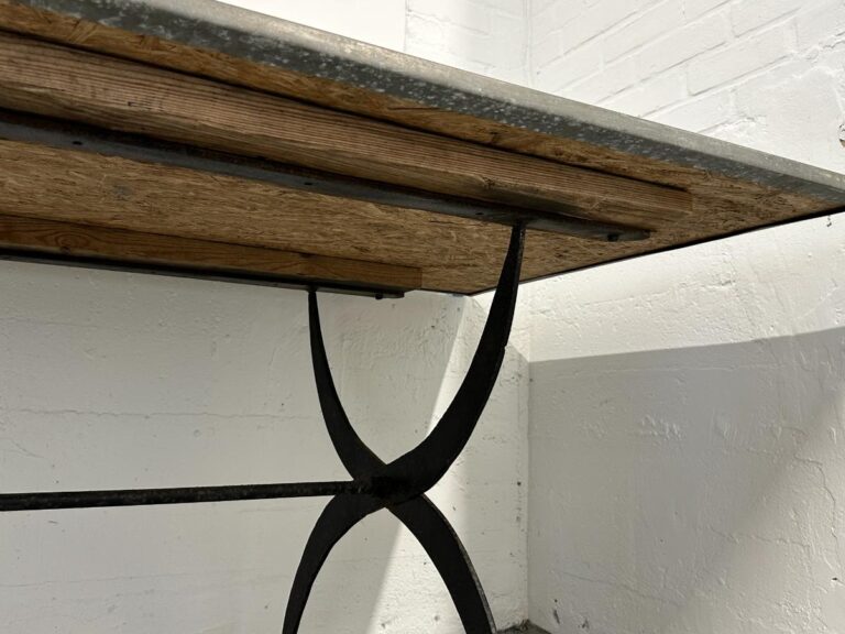 Close-up of a metal-framed table with a wooden top against a white brick wall.