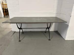 A metal table with a rectangular top and curved legs in an industrial-style room with white brick walls.