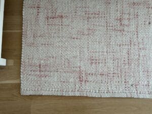A close-up of a woven rug with a pink and cream pattern on a wooden floor.