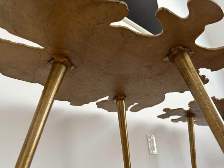 Low-angle view of a decorative gold table with irregular edges and thin gold legs against a white wall.