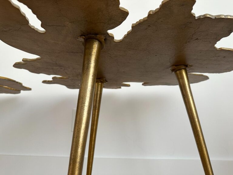 Close-up of gold metal table legs and textured tabletop with a leaf-like edge against a white background.