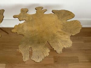 Gold metal side table with an abstract, leaf-like design on a wooden floor against a white wall.