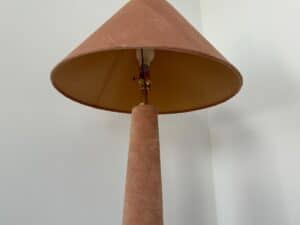 A brown lamp with a wide lampshade stands against a plain white wall, viewed from below.