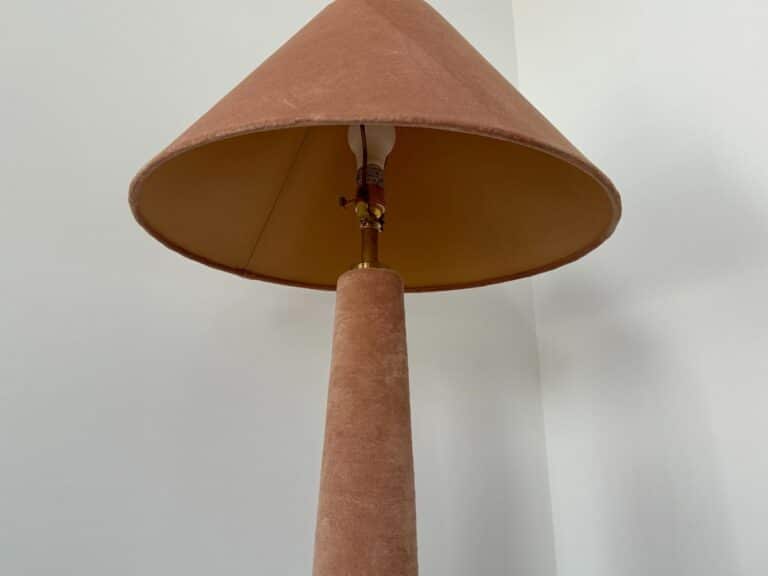 A brown lamp with a wide lampshade stands against a plain white wall, viewed from below.
