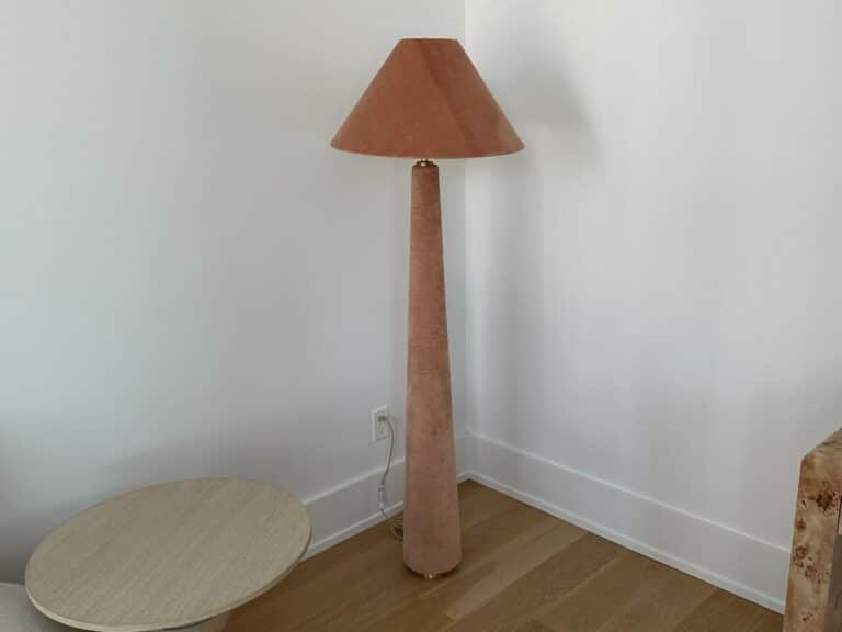 Tall pink floor lamp with a conical shade stands in the corner near a round light wood table.
