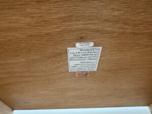 A wooden surface with an upside-down manufacturer’s label and warning sticker attached.