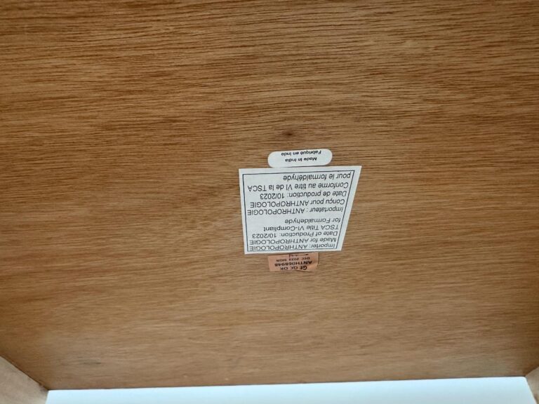 A wooden surface with an upside-down manufacturer’s label and warning sticker attached.